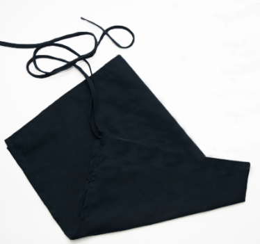 A black Prisma Bib Apron by Calderon Textiles is laid flat on a white surface, its waist ties loosely arranged above for added comfort.