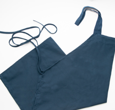 The Calderon Textiles Prisma Bib Apron, made of navy blue polyester with long neck and waist straps, is shown lying flat on a white surface for a comfortable fit.