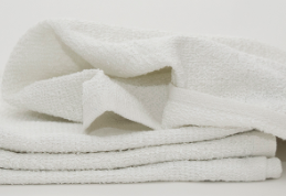 A stack of white MetroMop Ribbed towels by Calderon Textiles sits on a plain white background, with one towel partially unfolded on top—ideal for quick use in fast-paced environments.