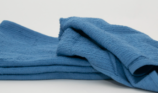 The Calderon Textiles MetroMop Ribbed, a folded blue towel with a textured surface, rests on a plain white background—ideal for quick use in fast-paced settings like Metro Mop facilities.