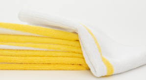 A stack of folded yellow cleaning cloths with a Calderon Textiles Microfiber Bar Ribbed white bar mop featuring a yellow stripe draped over the top, set against a white background.
