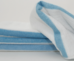 Three neatly folded Calderon Textiles Microfiber Bar Ribbed towels with light blue edges are stacked, with one partially unfolded and draped over the others on a plain white background.