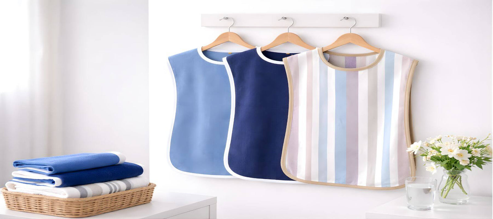 Adult hospital protectors and patient bibs hanging on wooden hangers with folded towels in a clean healthcare room setting