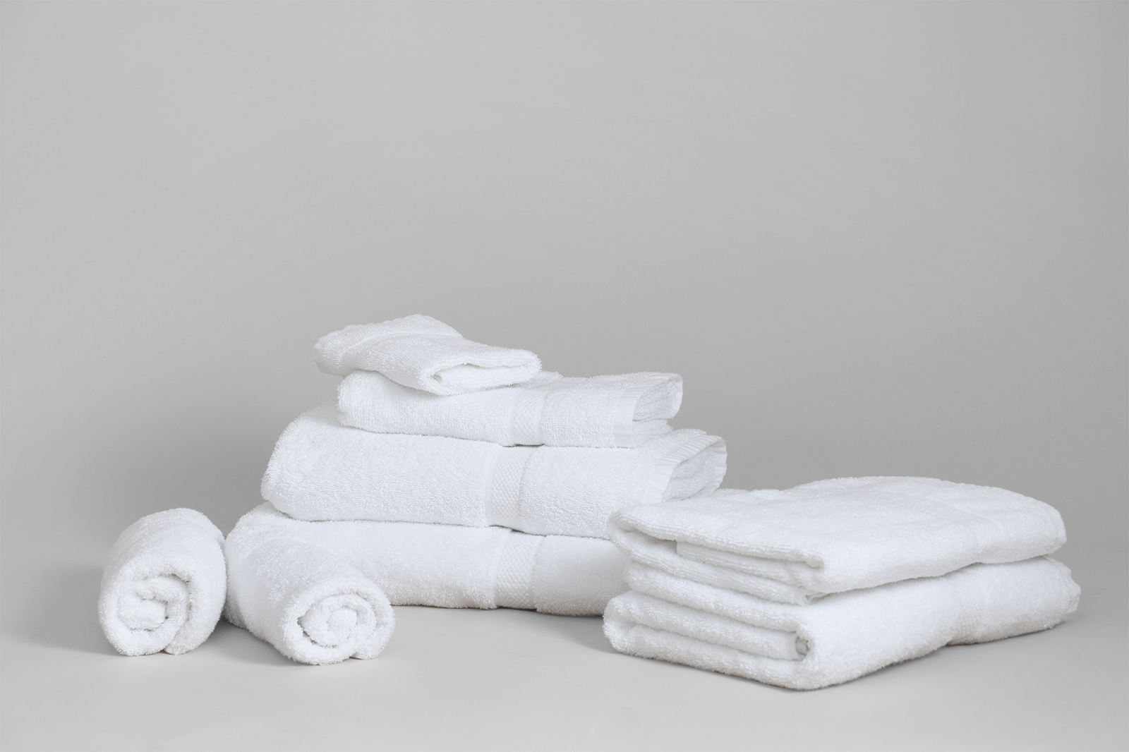 A neatly arranged set of KSE Beach Towel - Excellence Collection Hotel Towels, featuring stacked bath towels, folded towels, and two rolled soft ring-spun cotton hotel beach towels displayed against a light gray background.
