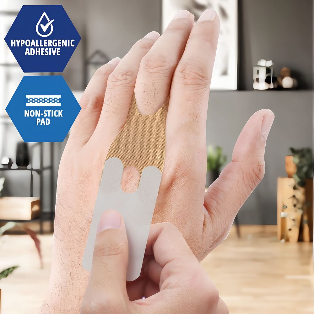 A person applies a Shield Line MedPride Sterile Fabric Knuckle Adhesive Bandage (1.5" x 3", skin-tone) to the back of their hand. Blue labels highlight Hypoallergenic Adhesive and Non-stick Pad. A living room is blurred in the background.