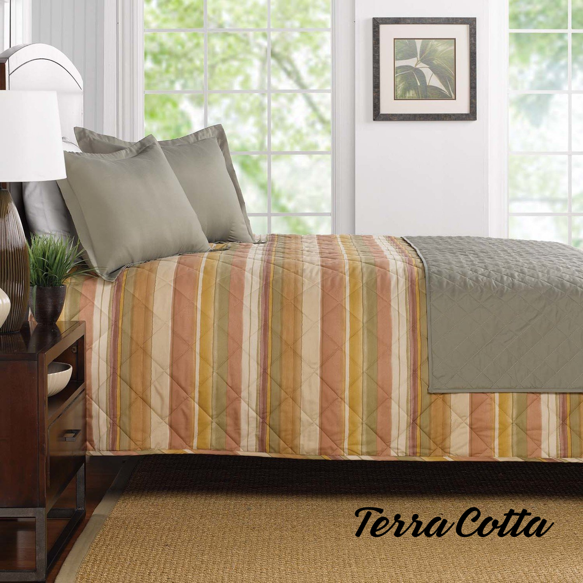 A neatly made bed with WestPoint Home's Comforters - WestPoint Hospitality - Pattern in terracotta, yellow, and beige stripes, topped with gray pillows and a gray blanket, creates a hotel look accented by large windows, wall art, and a plant.