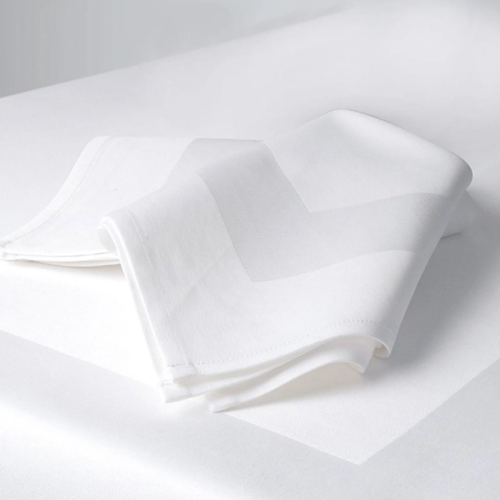 A neatly folded Ganesh Mills Napkin - Oxford Perfetta Satin Band sits on a matching white tablecloth, creating a clean and elegant look—ideal for those seeking quality cotton napkins or wholesale table linens.