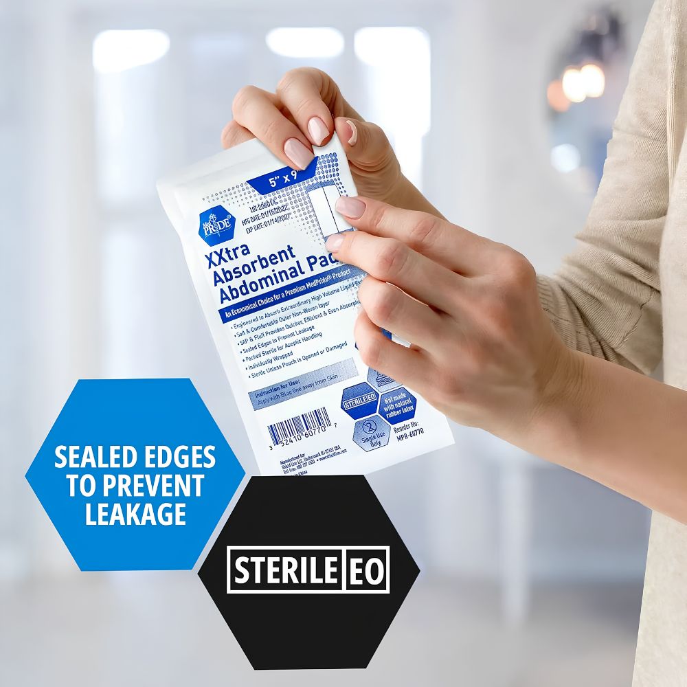 A person holds a Shield Line MedPride Extra Absorbent Abdominal Pad, 5x9 inches, sterile. Blue and black hexagons highlight sealed edges for leak prevention and Sterile EO. The white packet is in focus against a softly blurred background.