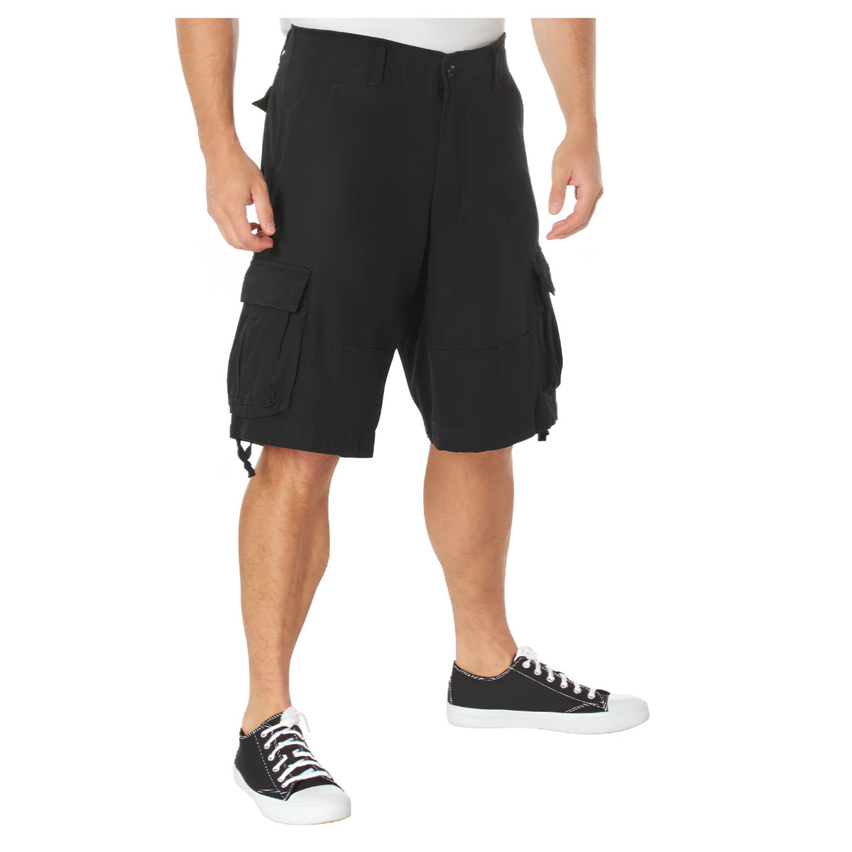 A person wearing Rothco Vintage Infantry Utility Cargo Shorts by Rothco, featuring multiple pockets, paired with black low-top sneakers with white soles, stands against a plain white background.