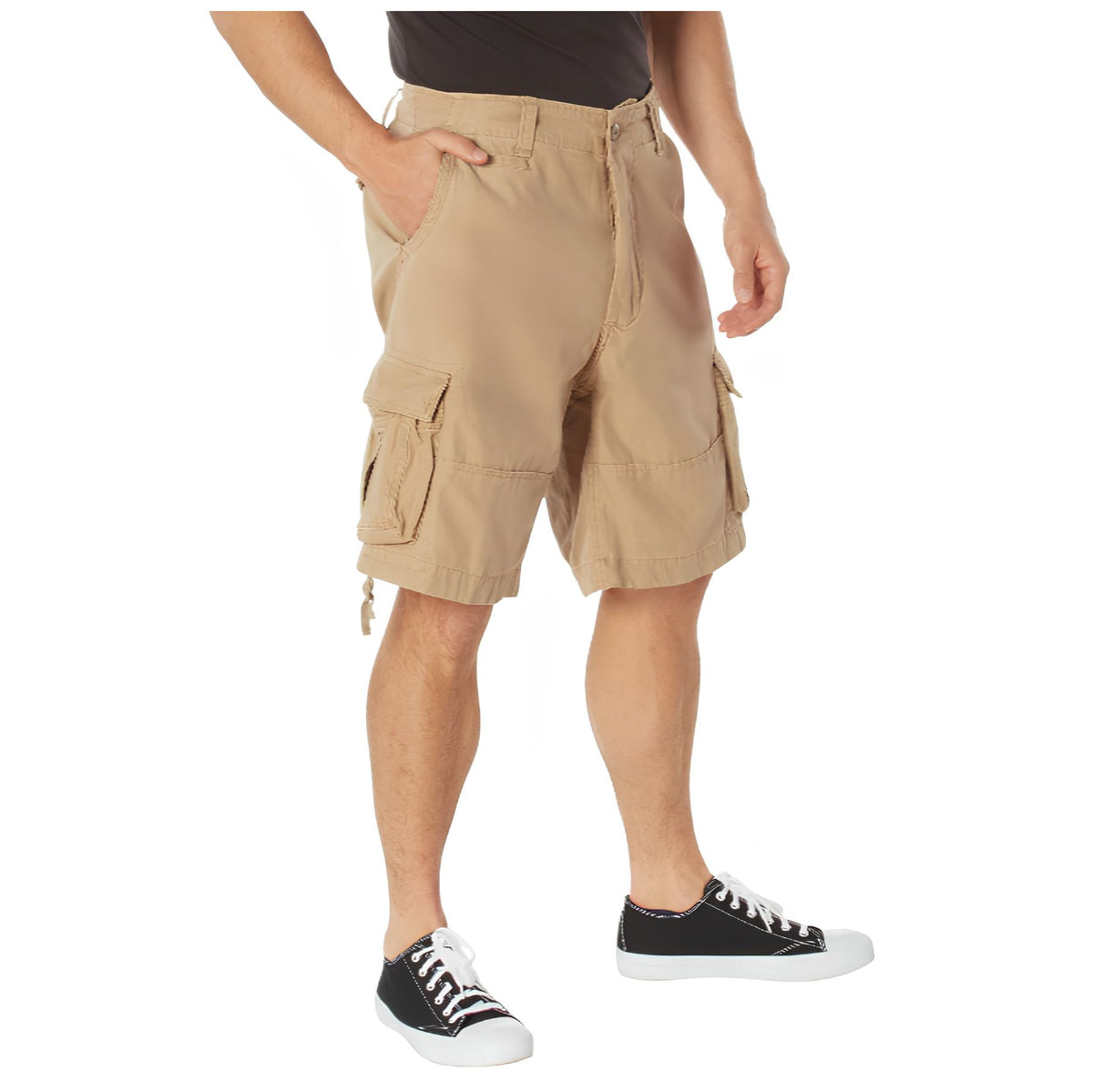 Someone stands against a white background wearing Rothco Vintage Infantry Utility Cargo Shorts by Rothco and black sneakers with white laces, one hand in their pocket.