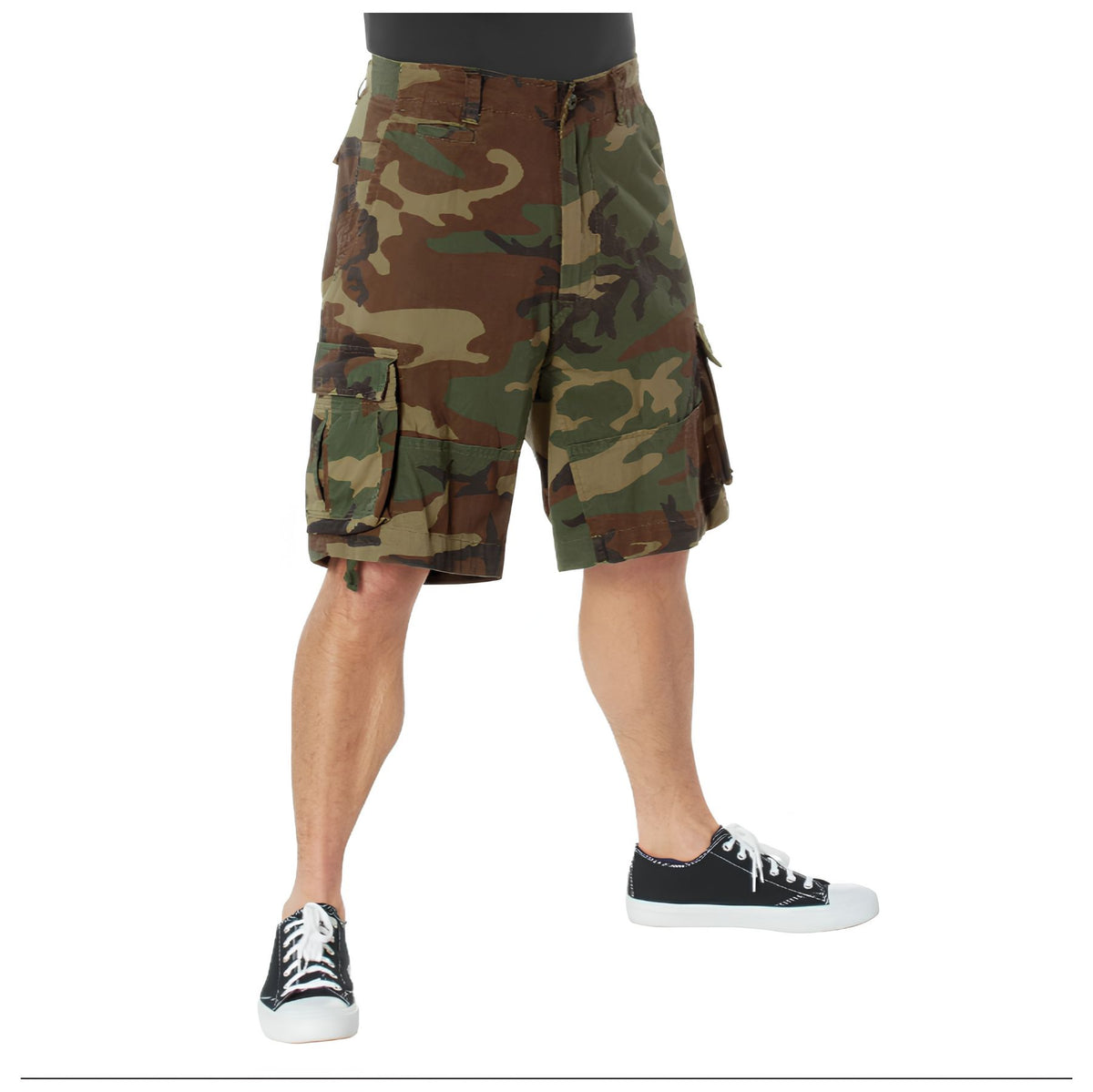 Wearing Rothco Vintage Infantry Utility Cargo Shorts and black low-top sneakers with white soles, a person stands against a white background; only the lower body is visible.