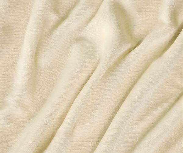A close-up of the Vellux Renew Chenille Blanket by WestPoint Home shows its light cream-colored, soft fabric with gentle, flowing folds and a smooth surface—hotel-quality comfort with subtle shadows highlighting the blanket’s plush drape.