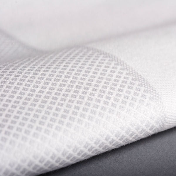 Close-up of Ganesh Mills Napkins - White/Black Oxford Satin Band Damask Table Linens, featuring a textured white fabric with a subtle diamond pattern, partially folded on a gray surface.