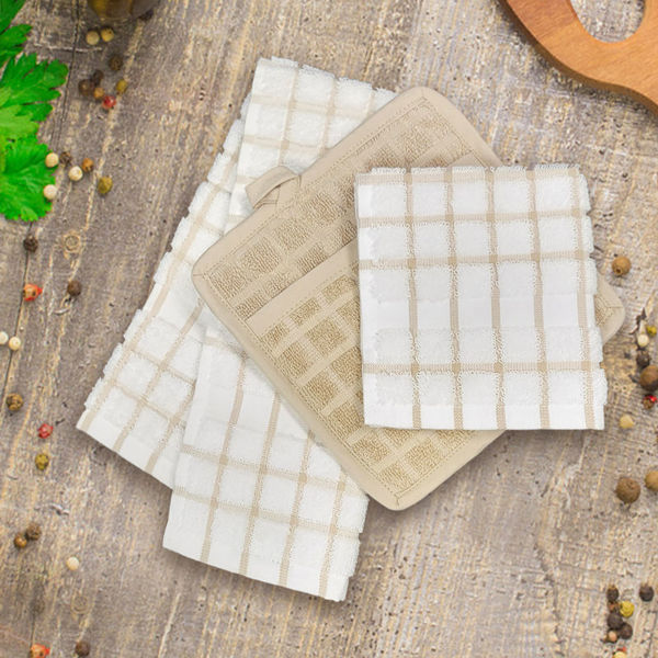 A Ganesh Mills Oxford Premium Dishcloth in a white and tan checkered pattern is displayed on a rustic wooden surface, accented by scattered peppercorns and a sprig of fresh parsley.