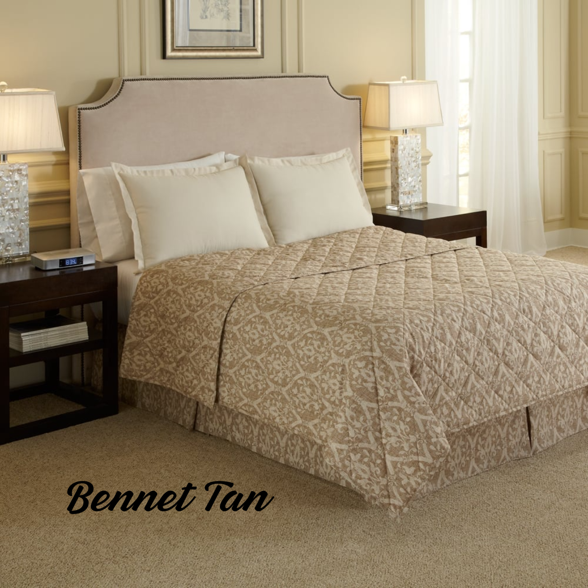 A cozy, well-lit bedroom features a neatly made bed with the WestPoint Home Comforters - WestPoint Hospitality - Pattern in beige, matching pillows, dark wood nightstands with lamps, and "Bennet Tan" text on the carpet.