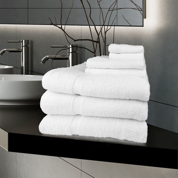 A stack of Ganesh Mills Hand Towel - White Oxford Gold Cam Towels sits on a black countertop in a modern bathroom with a sink, silver faucets, and a decorative branch in the background.