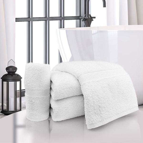 A stack of Ganesh Mills Bath Sheet / Pool Towel - White Oxford Regale Towels and a rolled towel rest on a gleaming surface, with a black lantern and tall window in the background.