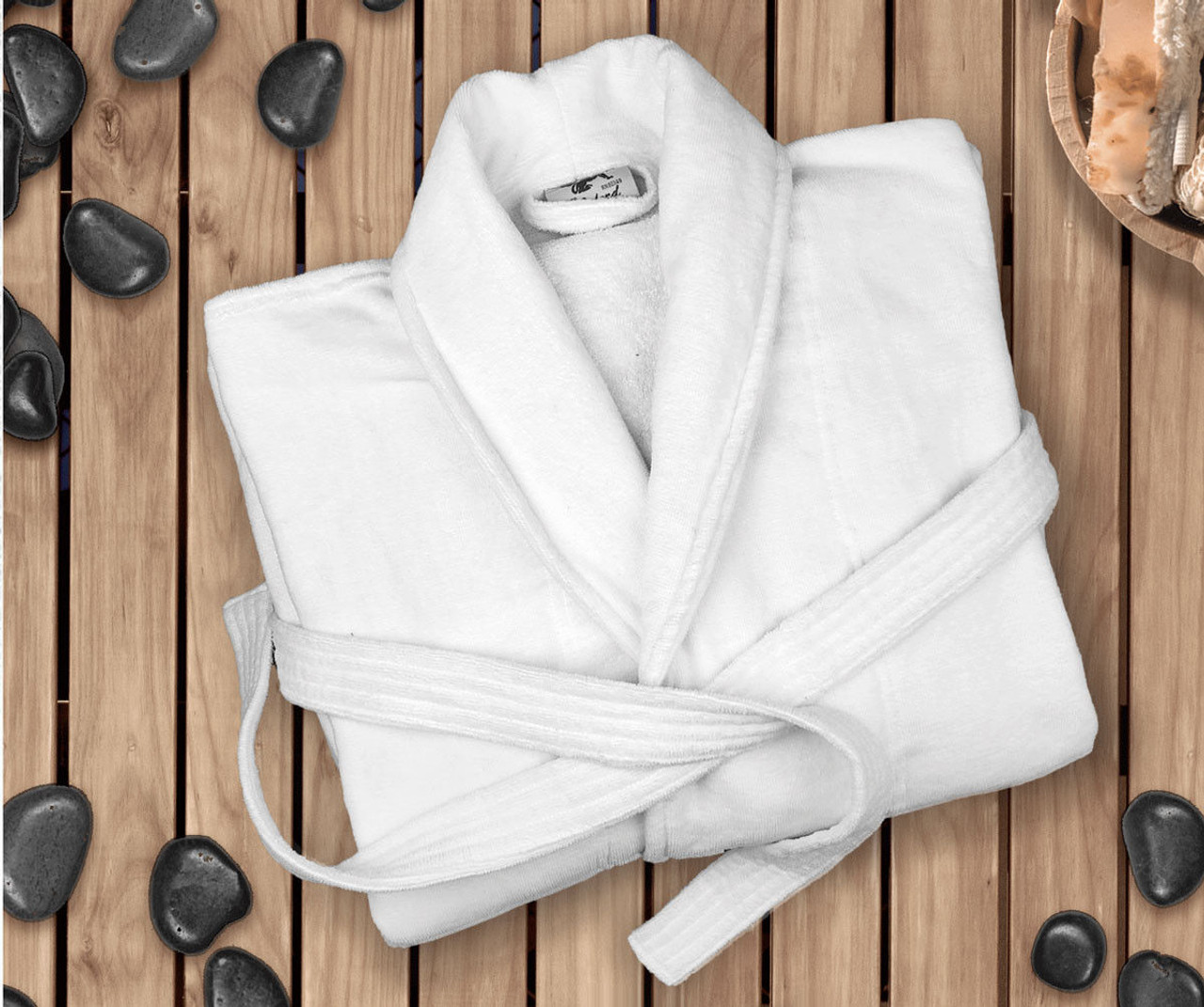 A Ganesh Mills White Replacement Belt for Oxford Velour Bathrobes is displayed on a wooden slatted surface, surrounded by black stones and a wooden bowl of towels for a calming, spa-like ambiance.