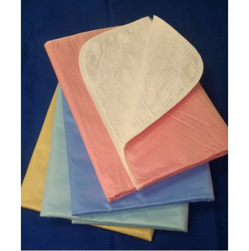 Four folded Intralin Super Twill PVC Incontinence Reusable Underpads in pastel pink, blue, light blue, and yellow are stacked on a dark blue surface. The top pink underpad is partially folded to show its white absorbent underside.