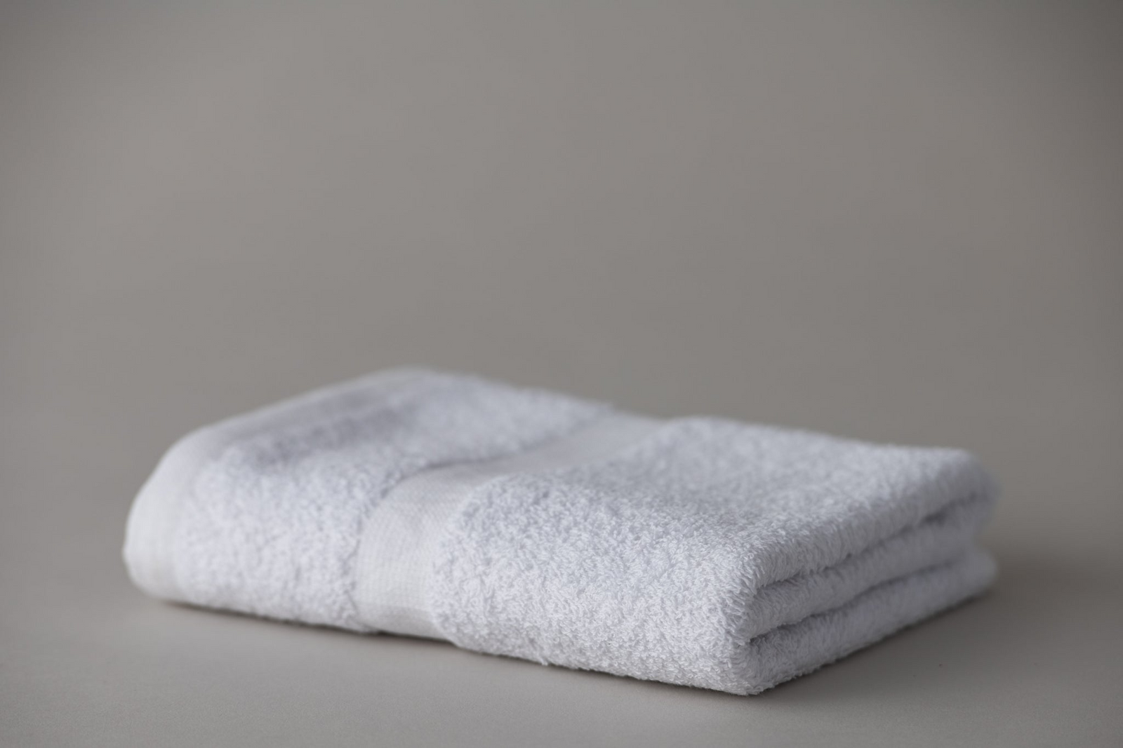 A Thomaston Cam Towel by Thomaston Mills is neatly folded on a plain, light gray surface, highlighting its soft texture, durable cotton quality, and simple, clean appearance.