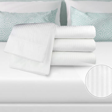 A stack of Ganesh Mills Fitted Sheets - Oxford T250 Tone On Tone Sateen Stripe rests on a made bed with white linens and blue patterned pillows; a close-up highlights the sheet’s subtle sateen stripe texture.