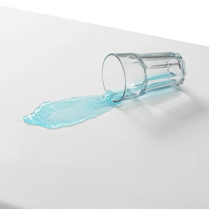 A clear glass spills light blue liquid on a white surface, but the Bargoose 3 Gauge Vinyl Fitted Cover (fits mattresses up to 9 deep) keeps everything underneath safe and dry.