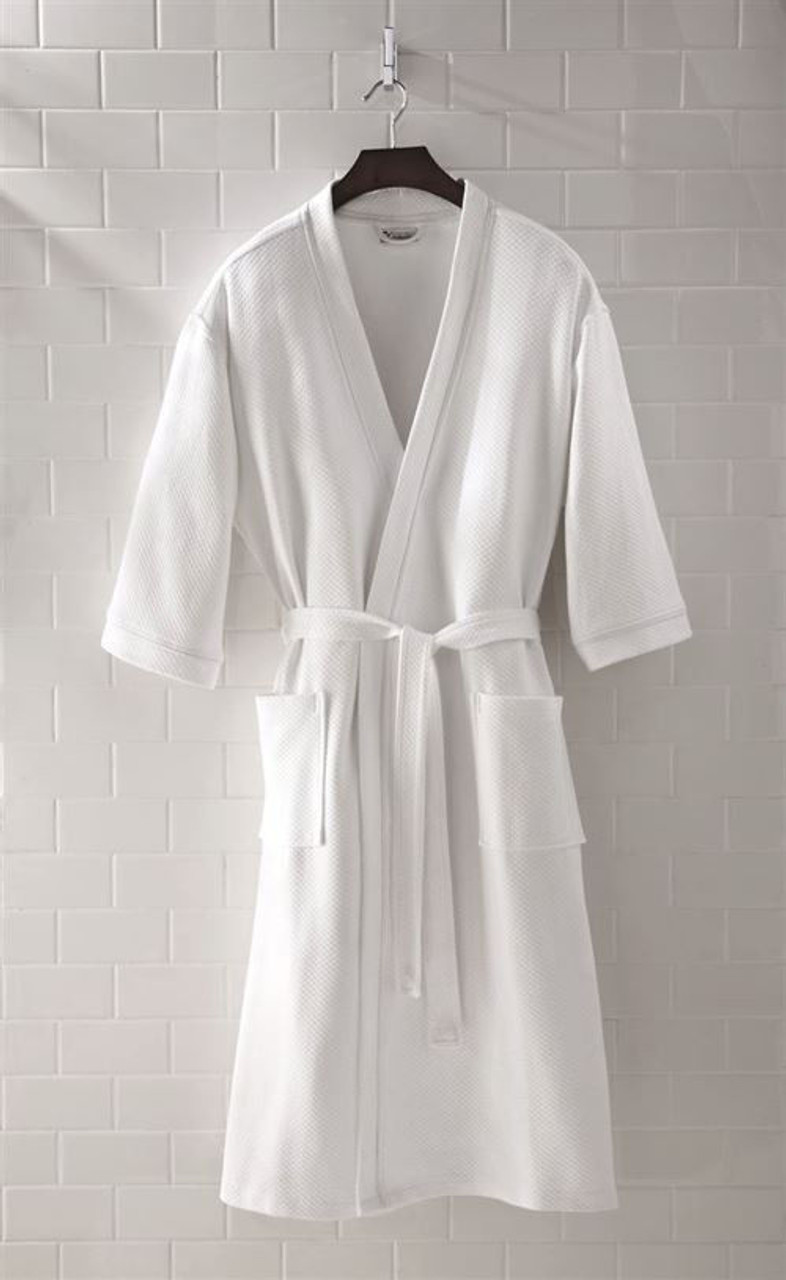 The 1Concier Bath Robes-emerald Kimono Robe, featuring a white waffle texture, belt, and two front pockets, hangs on a wooden hanger against a white tiled wall.