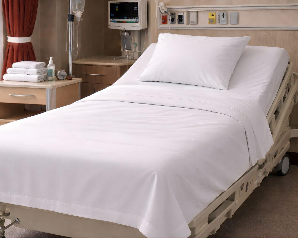 Adjustable hospital bed with clean white bed sheets, pillow linens and healthcare bedding in a modern patient room setting.