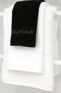 A neatly folded 1Concier Vanity Towel 100% Cotton hangs on a rack with a smaller black guest washcloth placed on top, featuring Refresh embroidered in cursive.