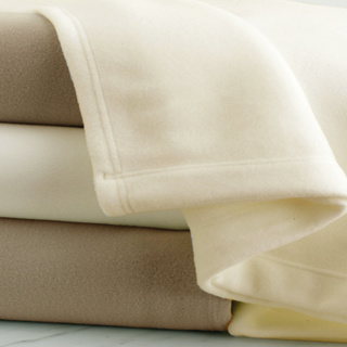 A close-up of three neatly folded Blanket Wonder throws by 1Concier, in cream, beige, and off-white, stacked together on a light surface.