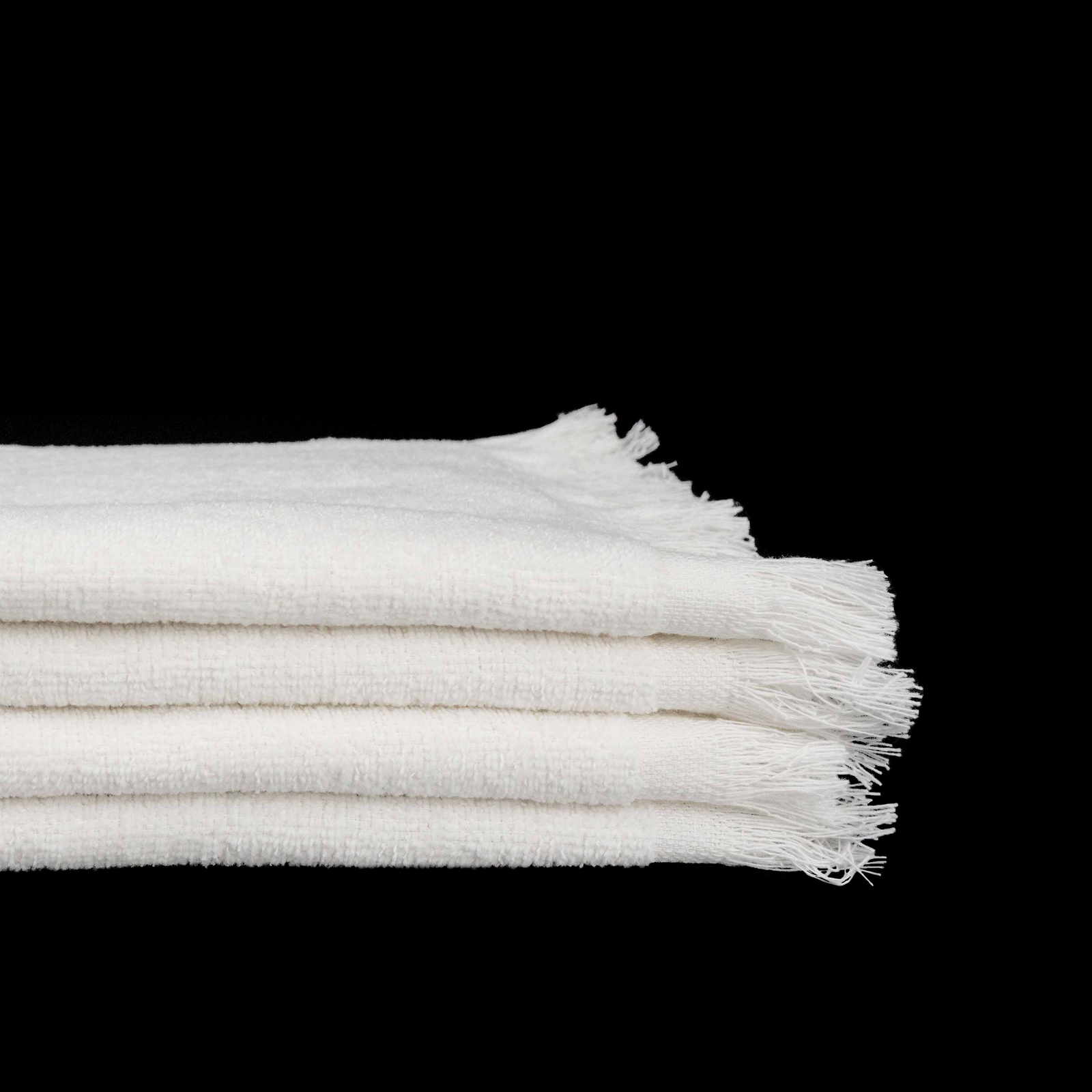A stack of three folded Bath Towel - Martex - Cam Towels by WestPoint Home, white cotton with frayed edges, set against a solid black background.
