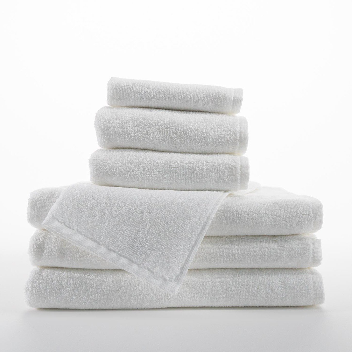 A stack of white Borderless Towel - Martex Luxe by WestPoint Home, made from 100% ring spun cotton, sits neatly on a white surface. The towels are fluffy, absorbent, and clean, with one towel draped over the stack.