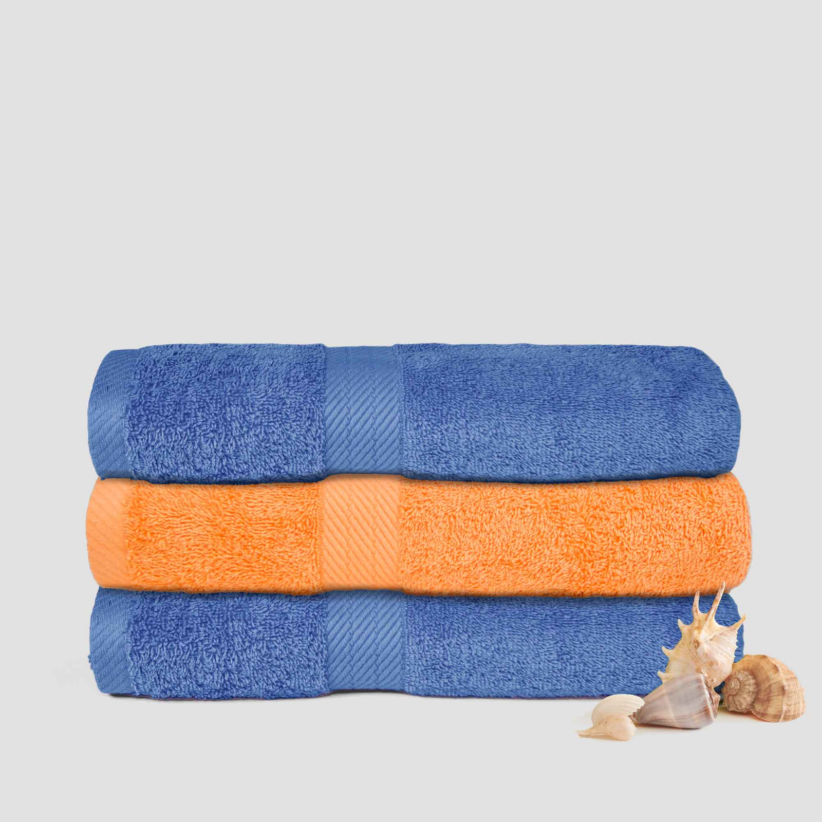 Two neatly folded Martex Staybright Pool Towels by WestPoint Home, one blue and one orange, are stacked together. Two seashells sit beside these bleach-friendly towels on a light gray surface.