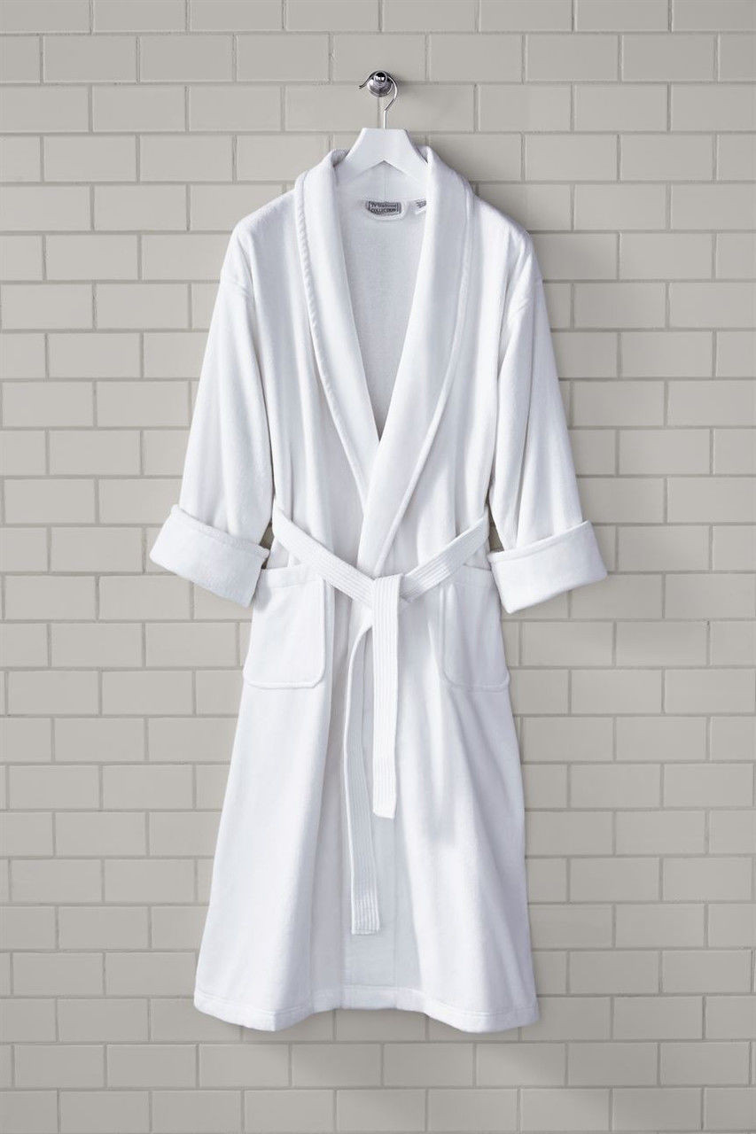 The 1Concier Traditional Kimono Robe, made of white cotton with a belt and rolled-up sleeves, hangs on a hook against a beige tiled wall.