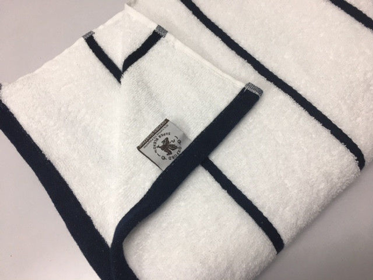 The Ganesh Mills Oxford Premium Horizontal Stripe Pool Towel, featuring black border stripes and a sewn-on rectangular label, is neatly folded on a flat, light-colored surface.