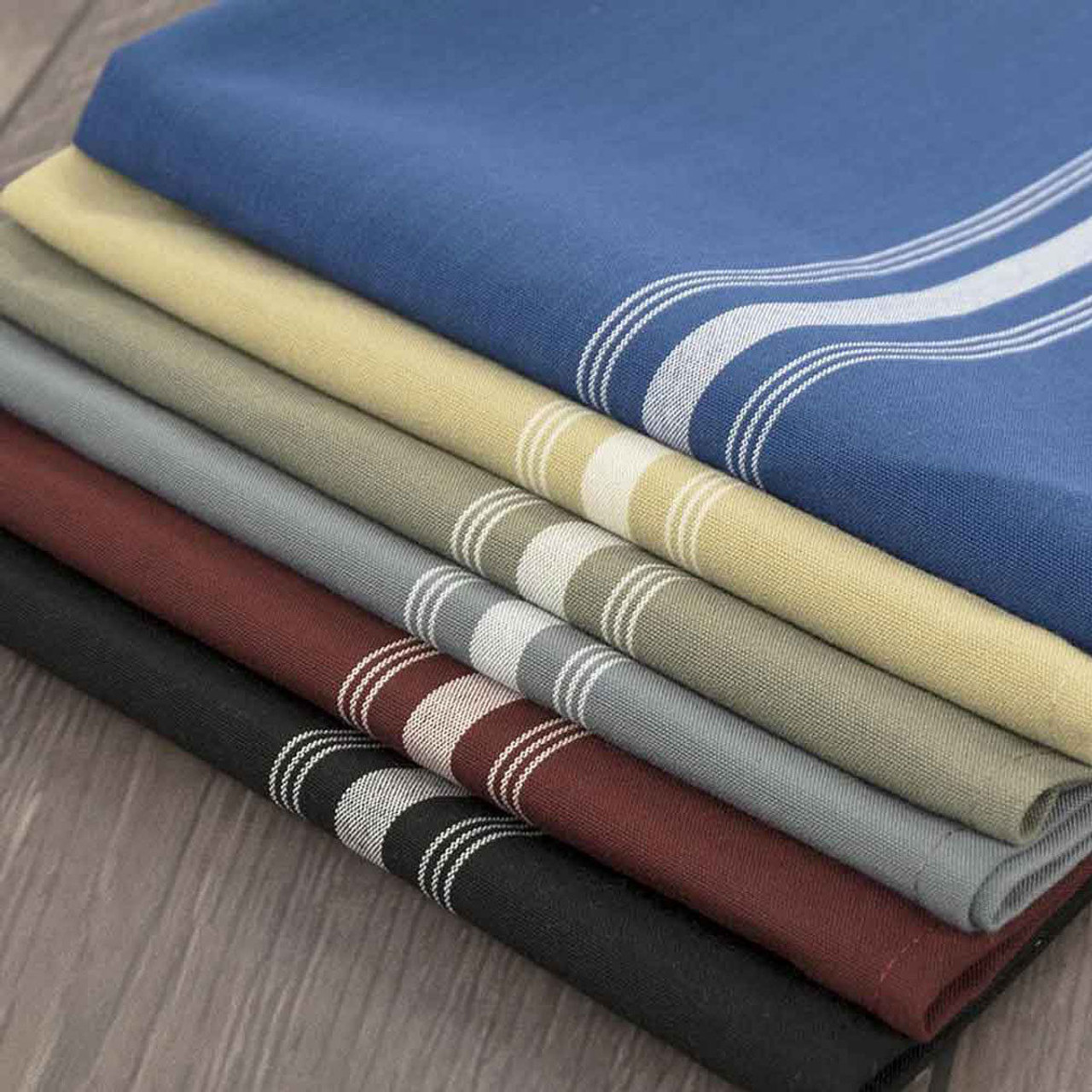 A stack of six Premier Bistro Napkins by 1Concier, in blue, beige, gray, and brown tones with simple parallel edge stripes, is neatly folded on a wooden surface.