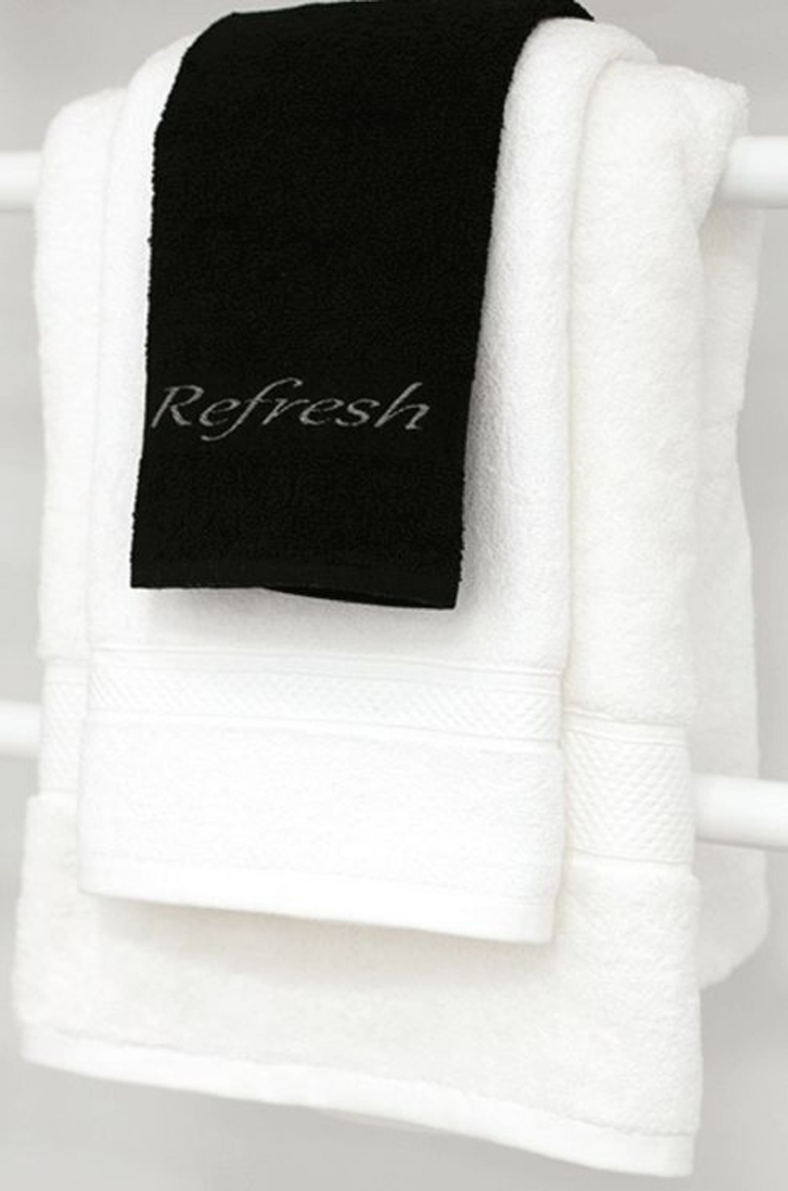 The Refresh Wash Cloth 100% Cotton by 1Concier, in black with Refresh embroidery, is neatly draped over a folded white towel, both hanging on a white towel rack.