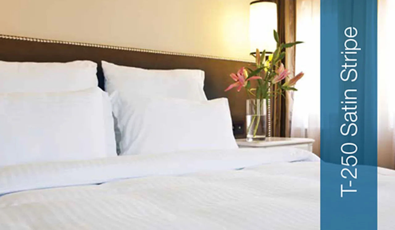 A neatly made bed features Thomaston Mills Wide Stripe 250 Thread Count Satin Stripe top sheet, pillows, a vase with pink flowers on the bedside table, and the product name displayed on a blue vertical banner.