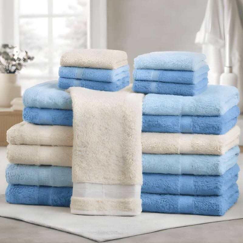 Stack of plush cotton bath towels in light blue, sky blue, and cream colors neatly arranged in a bright bathroom setting.