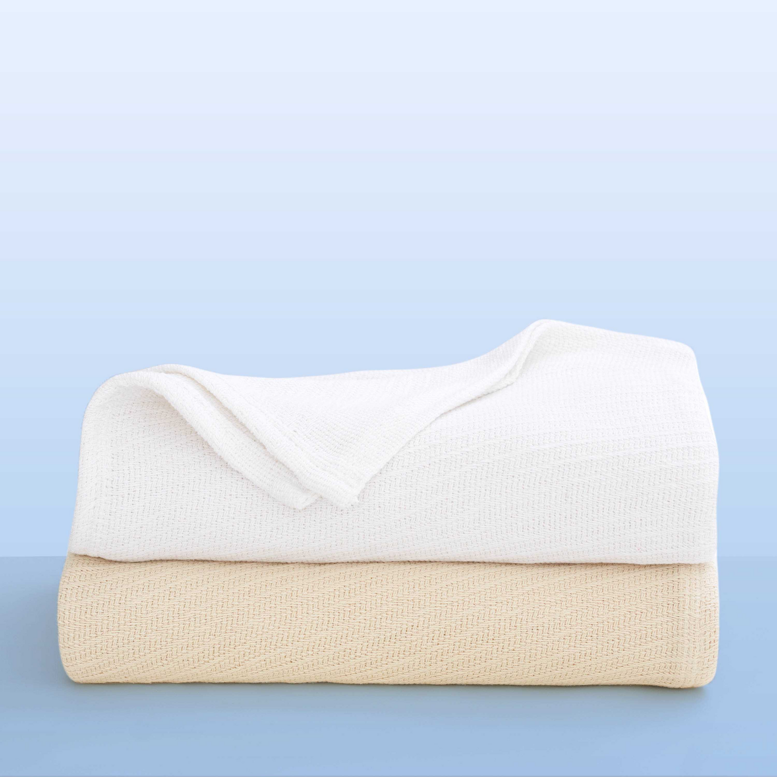 Two neatly folded Sovereign - Cotton Blankets by WestPoint Home, one white and one beige, are stacked on a light blue background. Both feature a soft, textured weave, making them ideal for hospitality blanket needs.