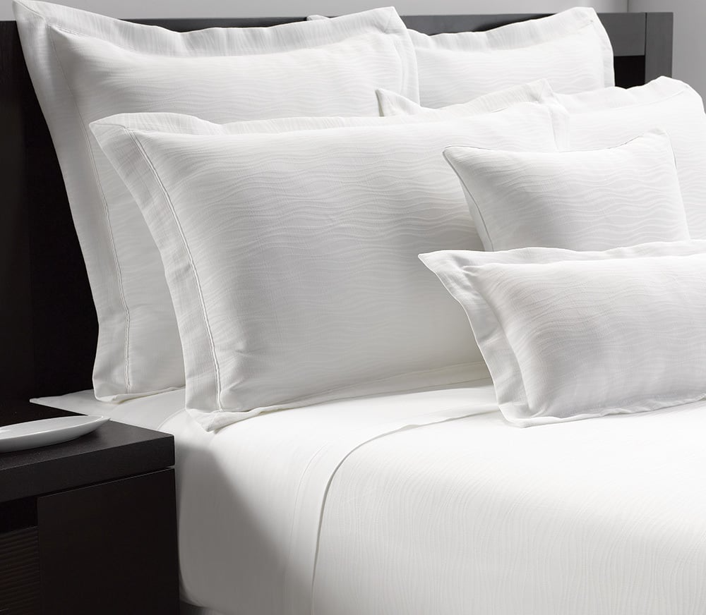 The Martex Wovens Decorative Top Sheet by WestPoint Home brings a clean, inviting look to your bed with crisp white jacquard fabric, paired with pillowcases and plush pillows against a dark headboard.