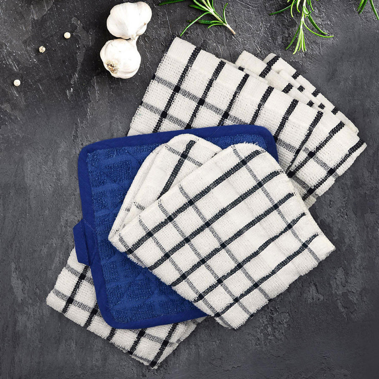 A flat lay of Ganesh Mills Dish Cloths - Colored/Checkered Pattern Oxford Kitchen Ensemble and a blue pot holder on a dark surface, surrounded by garlic cloves, peppercorns, and rosemary sprigs.