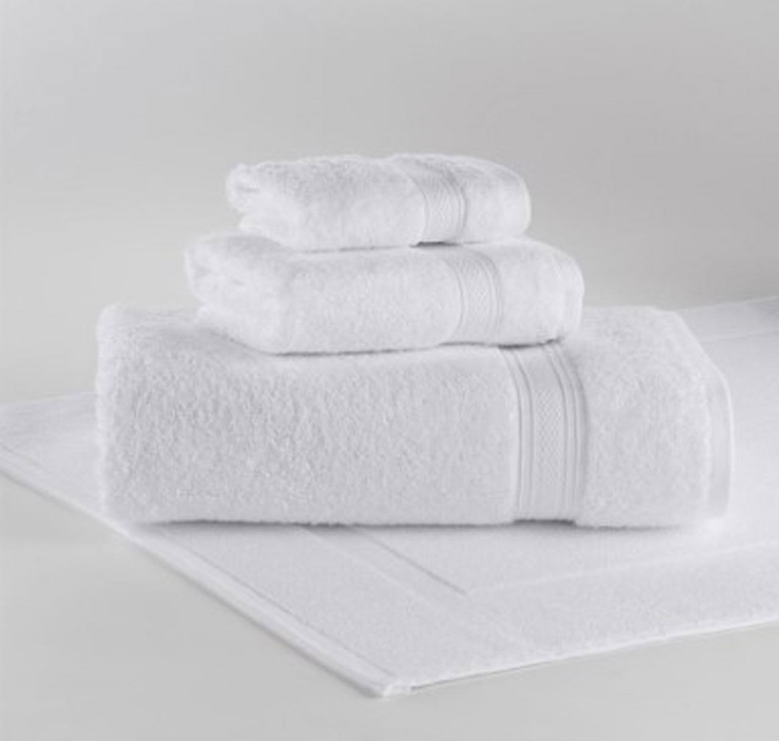 Three neatly folded white towels in various sizes, featuring a diamond weave dobby, are stacked atop a matching 1Concier Bath Mat 100% Cotton, all against a plain light background.