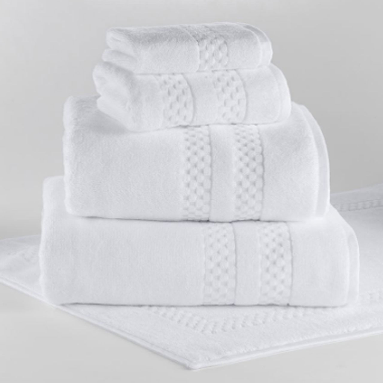 A neatly stacked set of four 1Concier Hand Towel Vip Terry 100% Cotton towels, each with a textured band pattern and classic finish, displayed on a white surface with a matching white bath mat underneath.