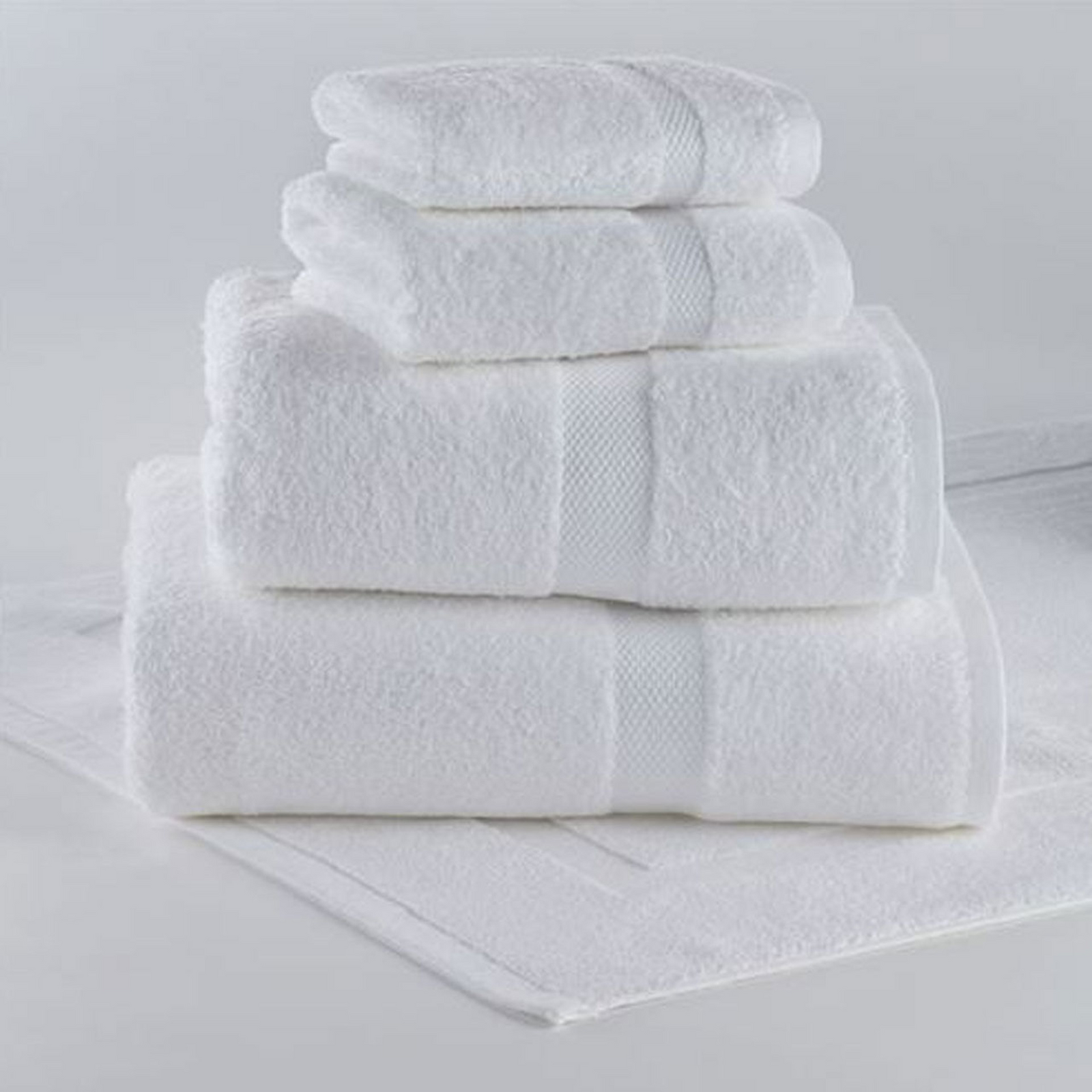 A neatly stacked pile of four Ruby Wash Cloths by 1Concier, made from 100% cotton with a plush feel and rice weave border, displayed on a matching white bath mat against a plain light background.