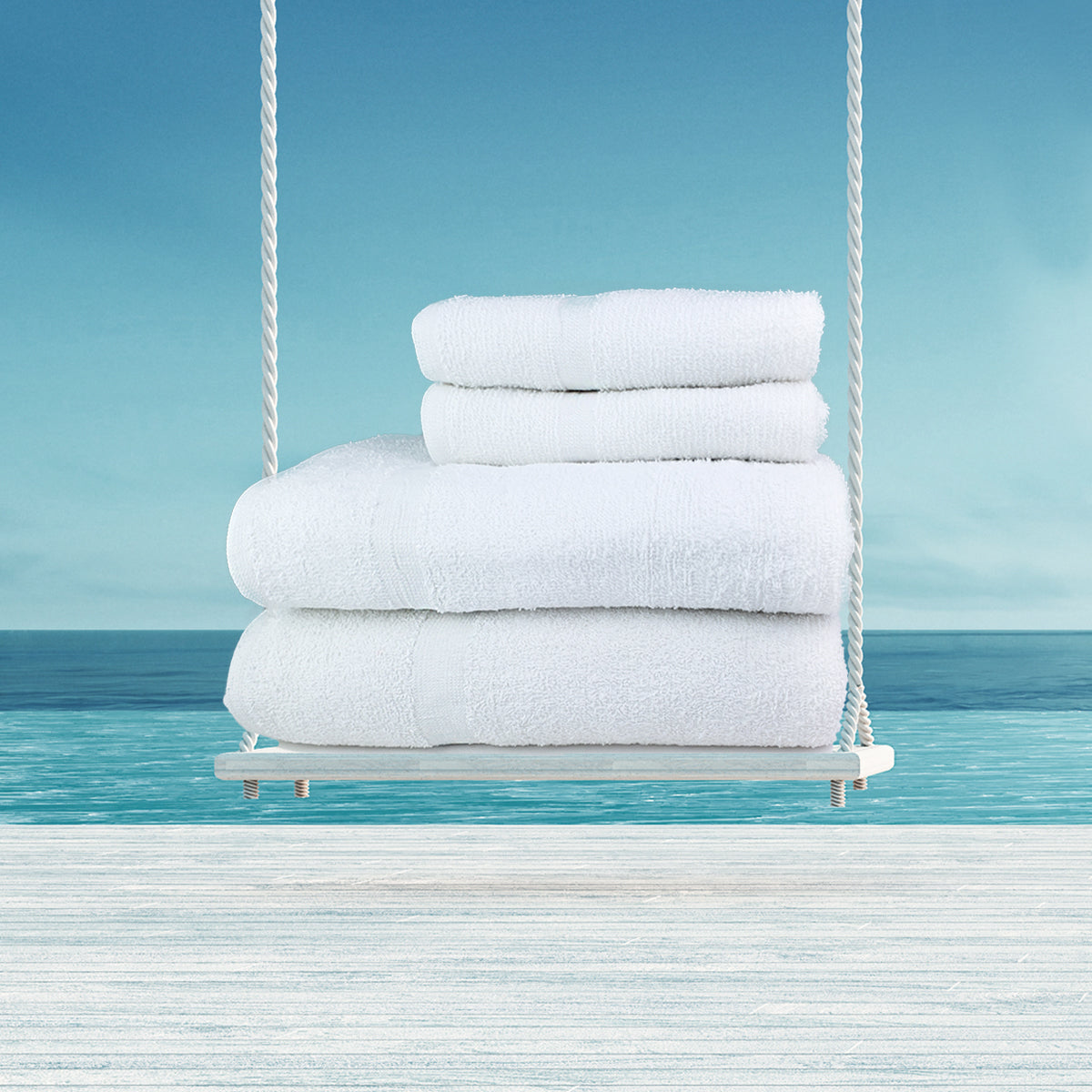 The Ganesh Mills Hand Towel - White Oxford Classic Bronze is neatly folded on a wooden swing, set against a calm blue ocean and sky, creating a serene and relaxing atmosphere.