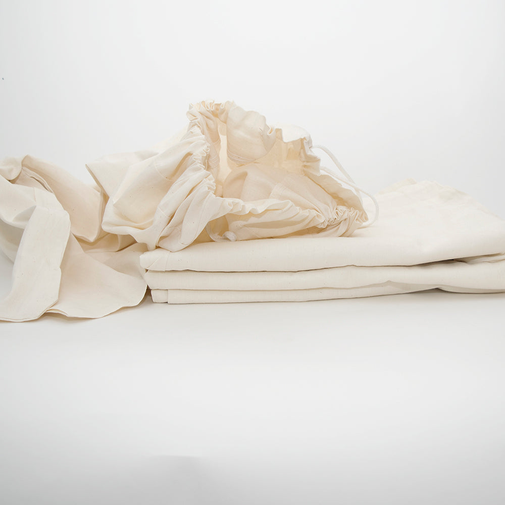 A cream-colored Laundry Bag by Calderon Textiles, featuring folded fabric pieces including a drawstring bag, displayed on a white background.
