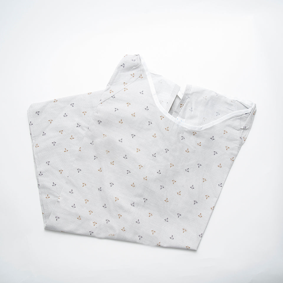 The Calderon Textiles Back-Tie Patient Gown is shown folded on a white background, featuring a white fabric with small floral prints in light brown and gray.
