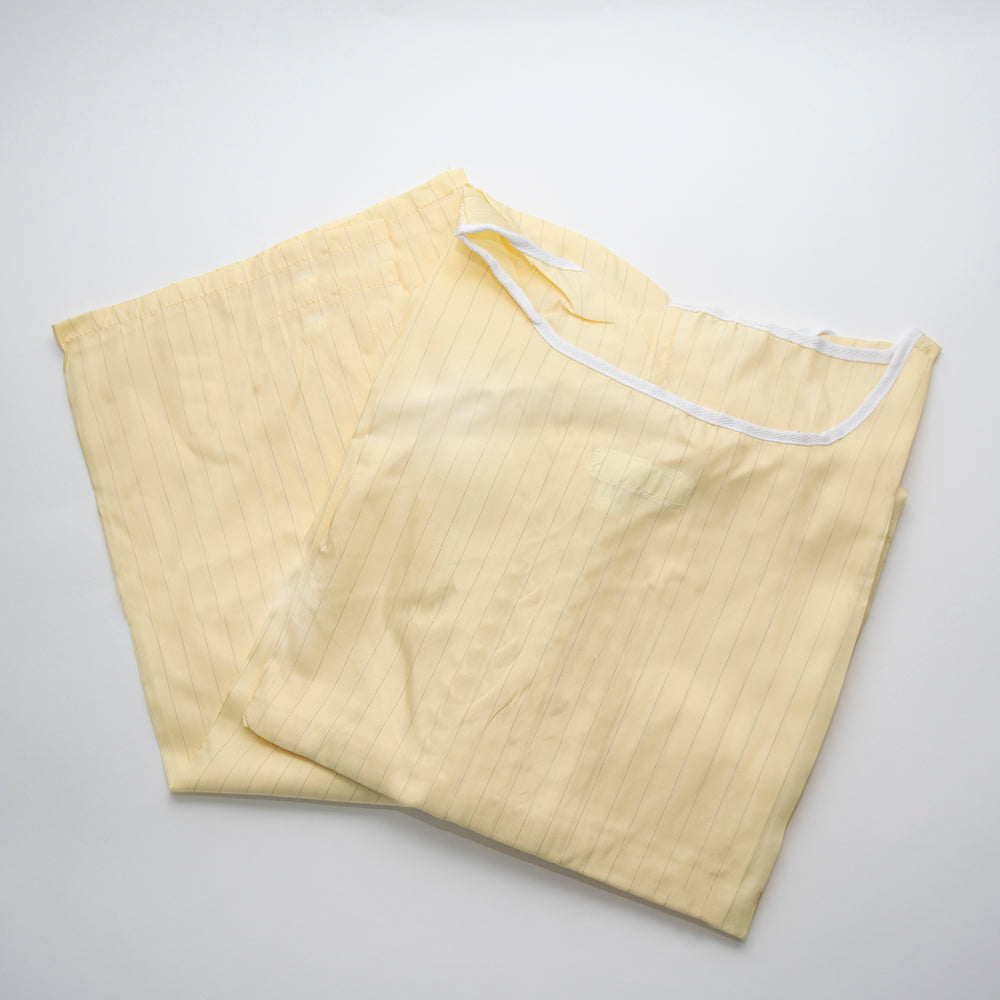 Two light yellow Calderon Textiles PPE Isolation Gowns, with subtle vertical stripes like patient gowns, are laid flat on a white surface. One slightly overlaps the other and features a white drawstring closure at the top.