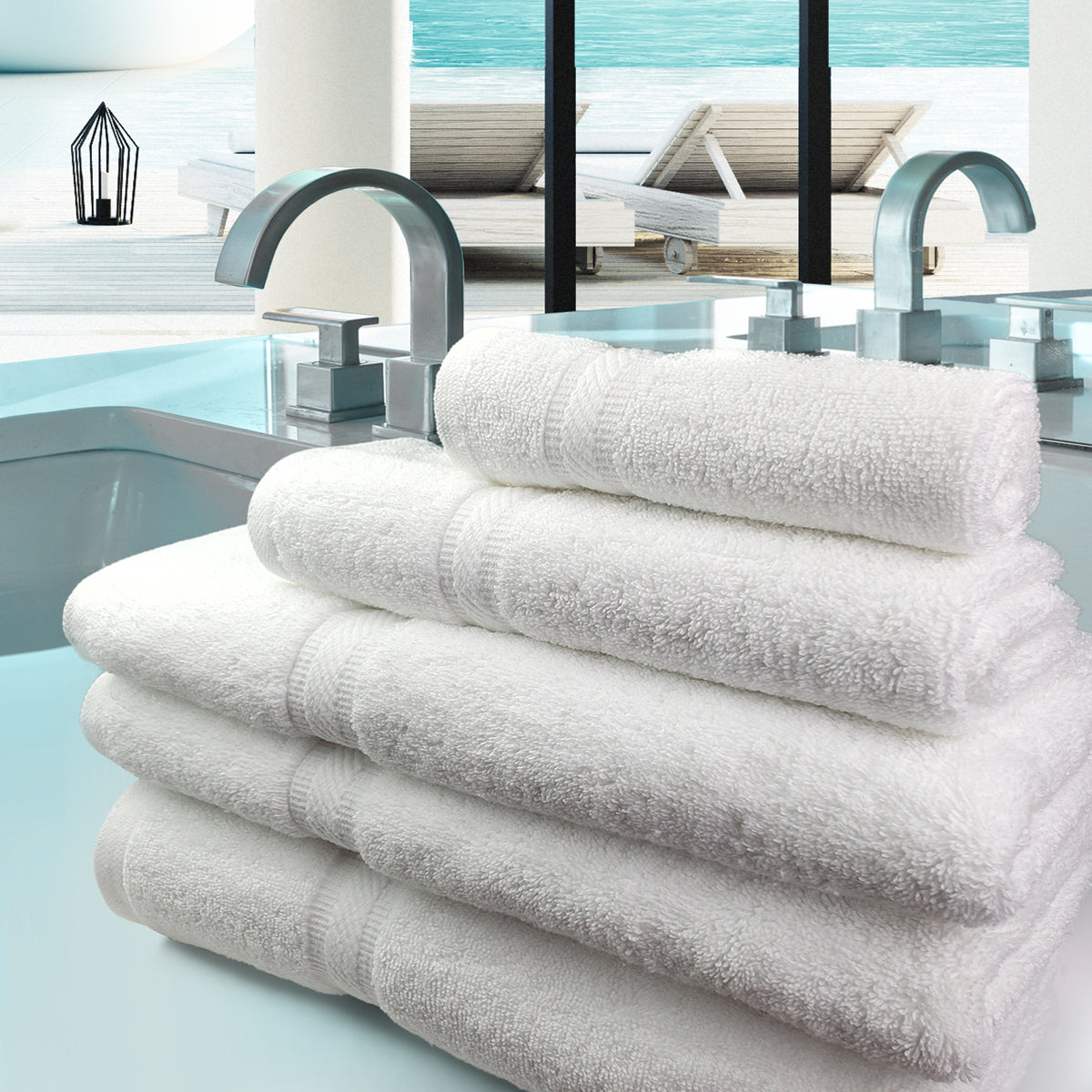 A stack of six white Oxford Forza Washcloths by Ganesh Mills is neatly arranged on the edge of a modern bathtub, with sleek silver faucets and a view of a swimming pool and lounge chairs through large windows.